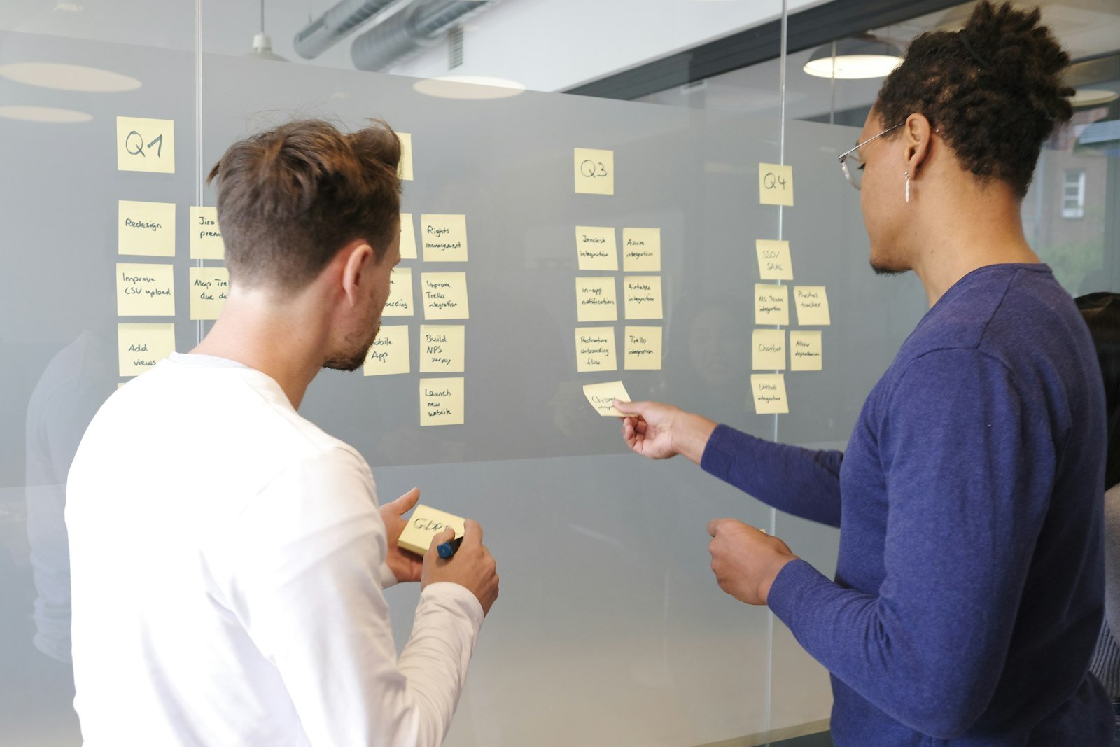 Two people organizing a quarterly plan with sticky notes on a glass wall