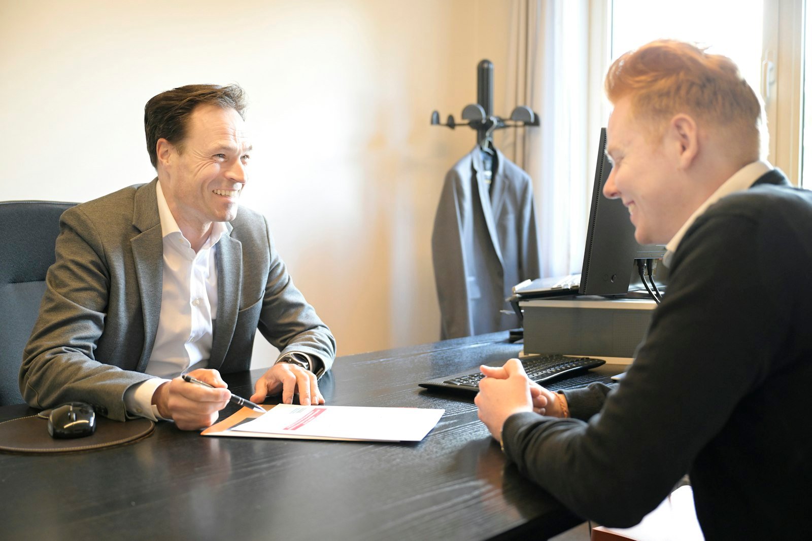 Two professionals smiling across an office desk while reviewing a document