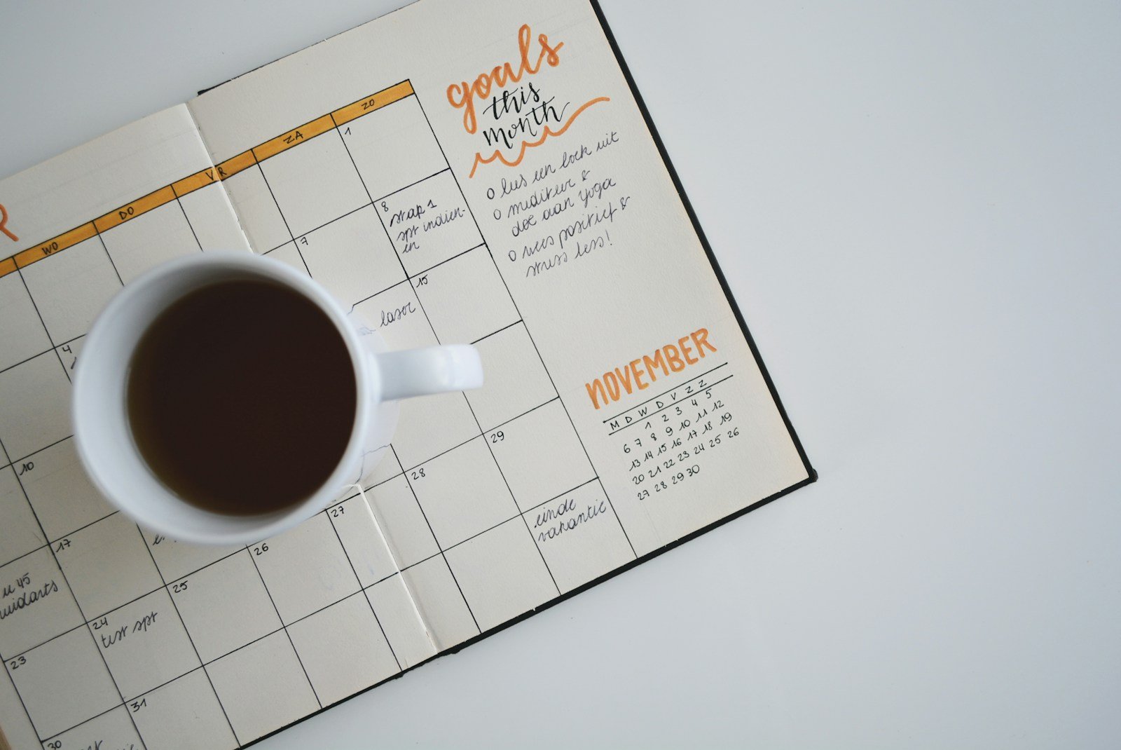 An open planner with a cup of coffee and monthly goals written in orange